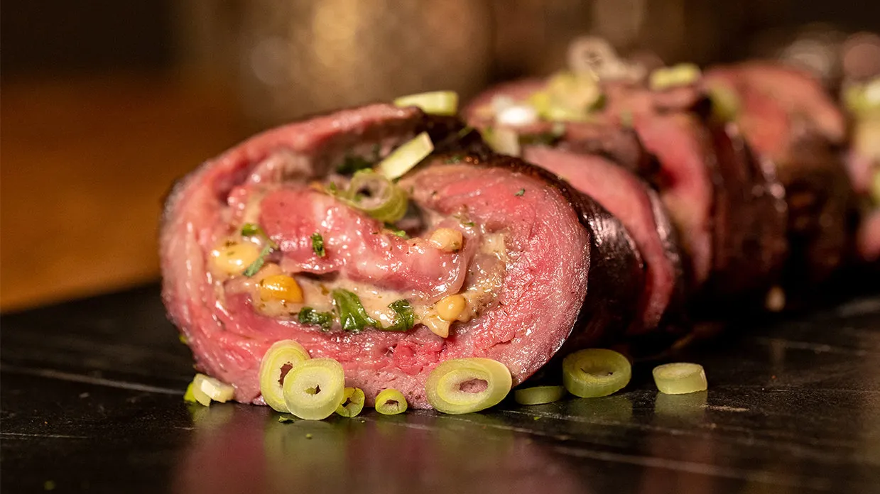Aangesneden bavette rollade gevuld met carpaccio ingrediënten, geserveerd op een houten plank