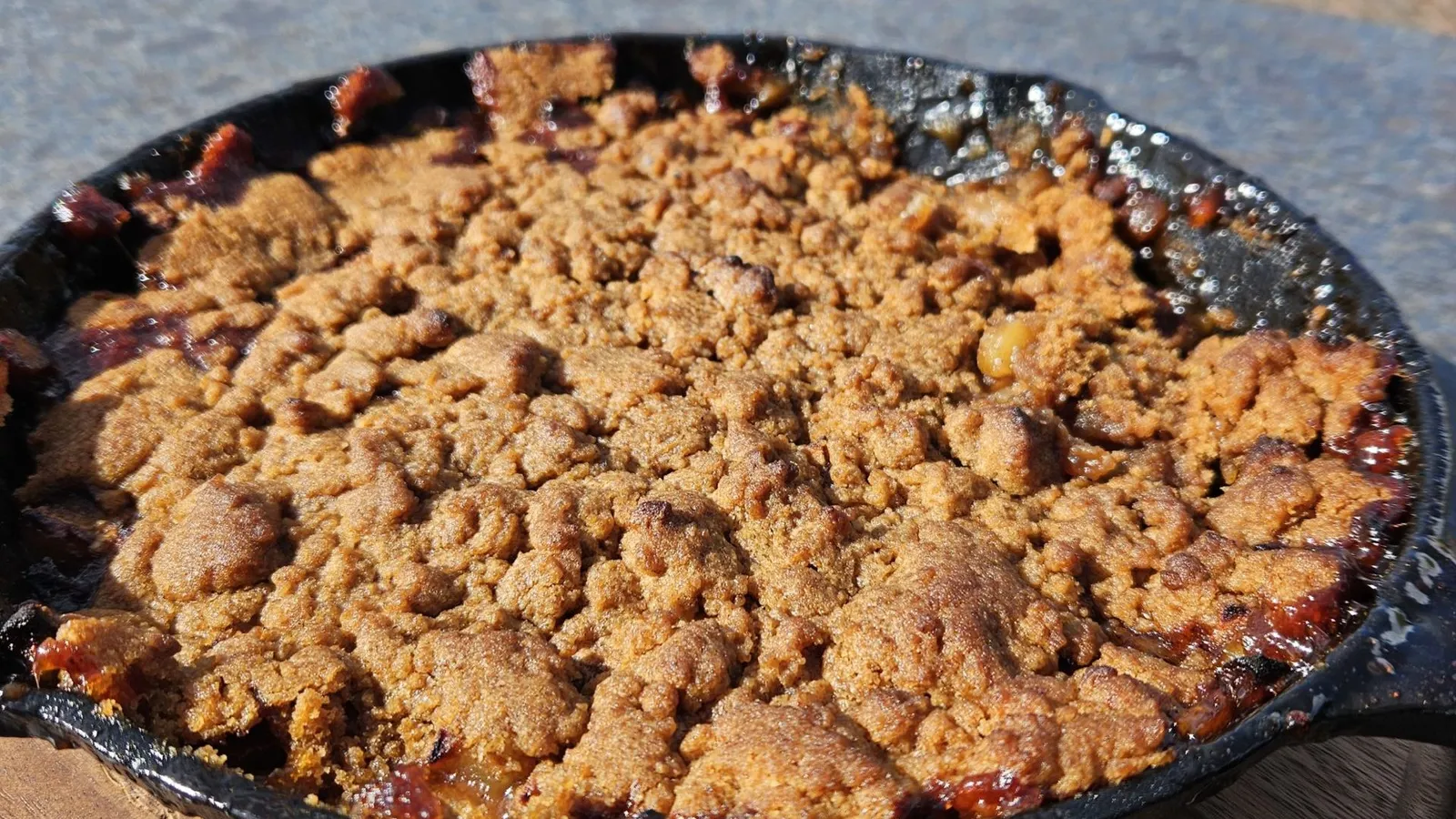 Een skillet met een goudbruin gebakken Brown Betty dessert met appels en kruimels, direct van de barbecue.