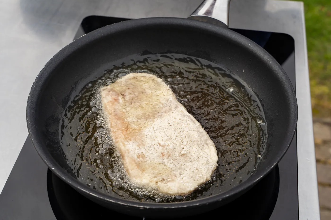 Kalfsschnitzel net in de hete olie gelegd om krokant te bakken