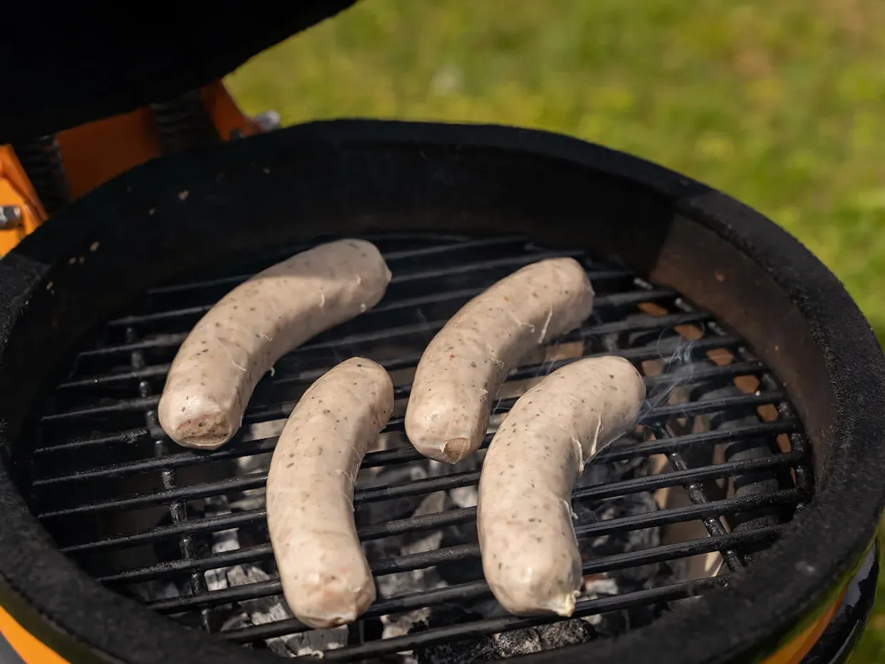 Rustieke worstjes die op het rooster van de barbecue liggen boven direct vuur