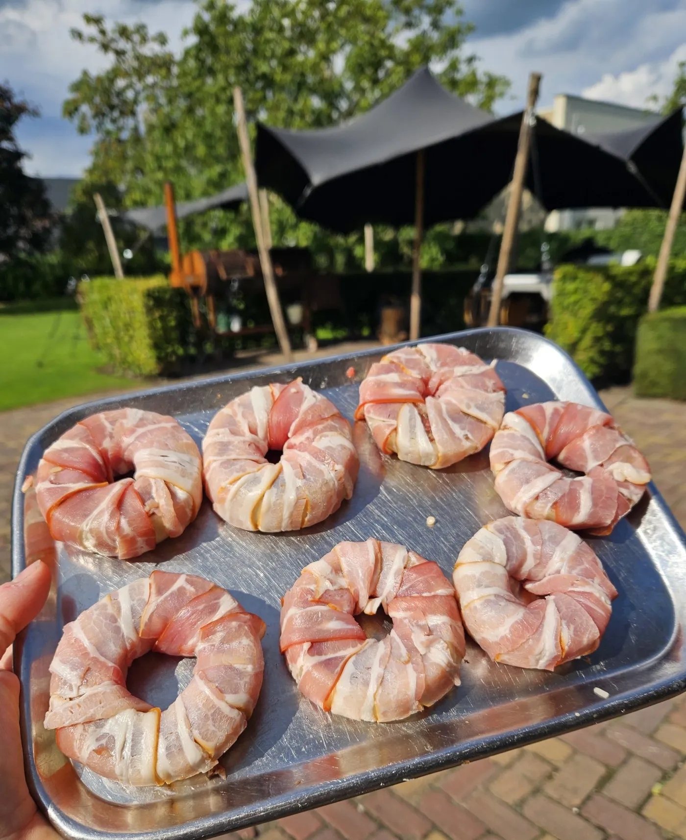 Spek-omwikkelde uienringen garen op het rooster van de barbecue.