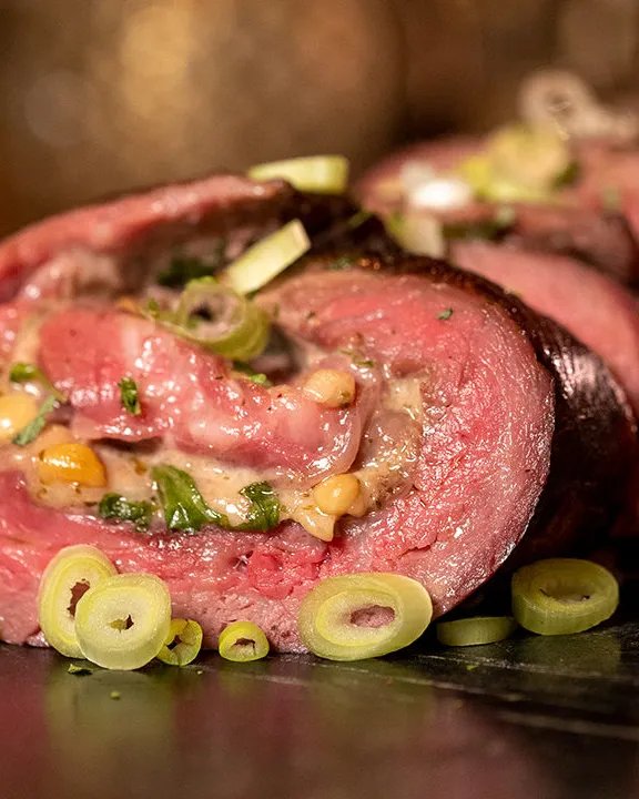Aangesneden bavette rollade gevuld met carpaccio ingrediënten, geserveerd op een houten plank