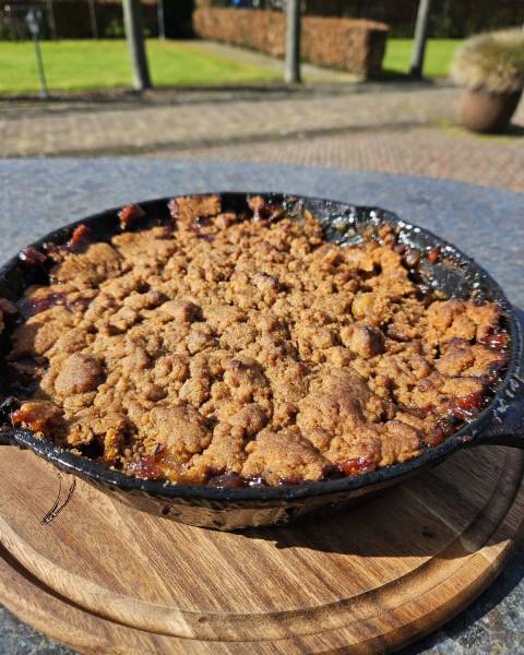 Een skillet met een goudbruin gebakken Brown Betty dessert met appels en kruimels, direct van de barbecue.